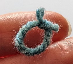 A small blue stitch marker made from yarn tied into a circle.
