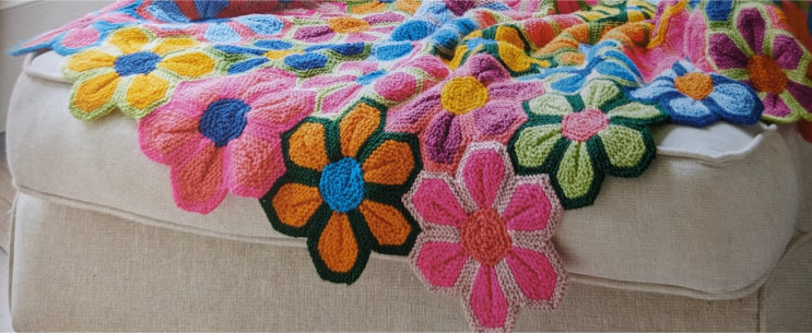A cropped image of a blanket made of multicolored interlocking flower shapes, laying across an armchair.