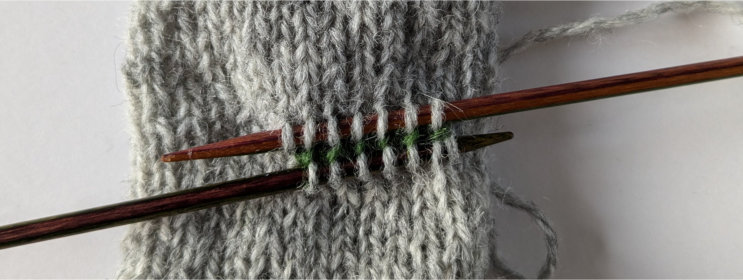 Double pointed needle used to pick up stitches above, below and to the side of the waste yarn stitches