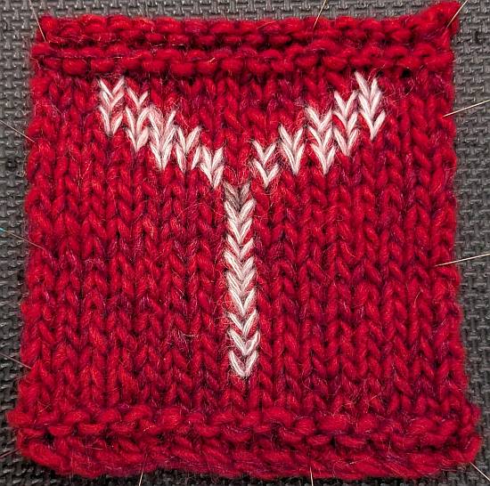 A red swatch made with bulky yarn and a botanical motif made by Swiss darning on top of the fabric