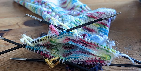 Multicolored socks in progress on double pointed needles, with yarn markers between every few stitches!